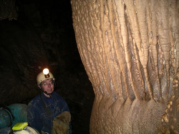 Photo of a caver standing next to a rock formation with a regular
							vertical pattern