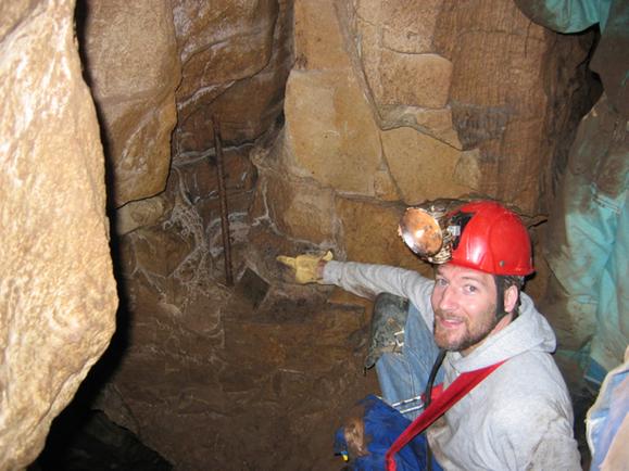 Photo of the author pointing to an iron bar set in an alcove of the
							cave