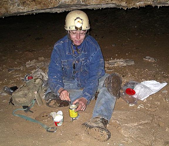 Photo of a caver seated on the ground eating from a can
